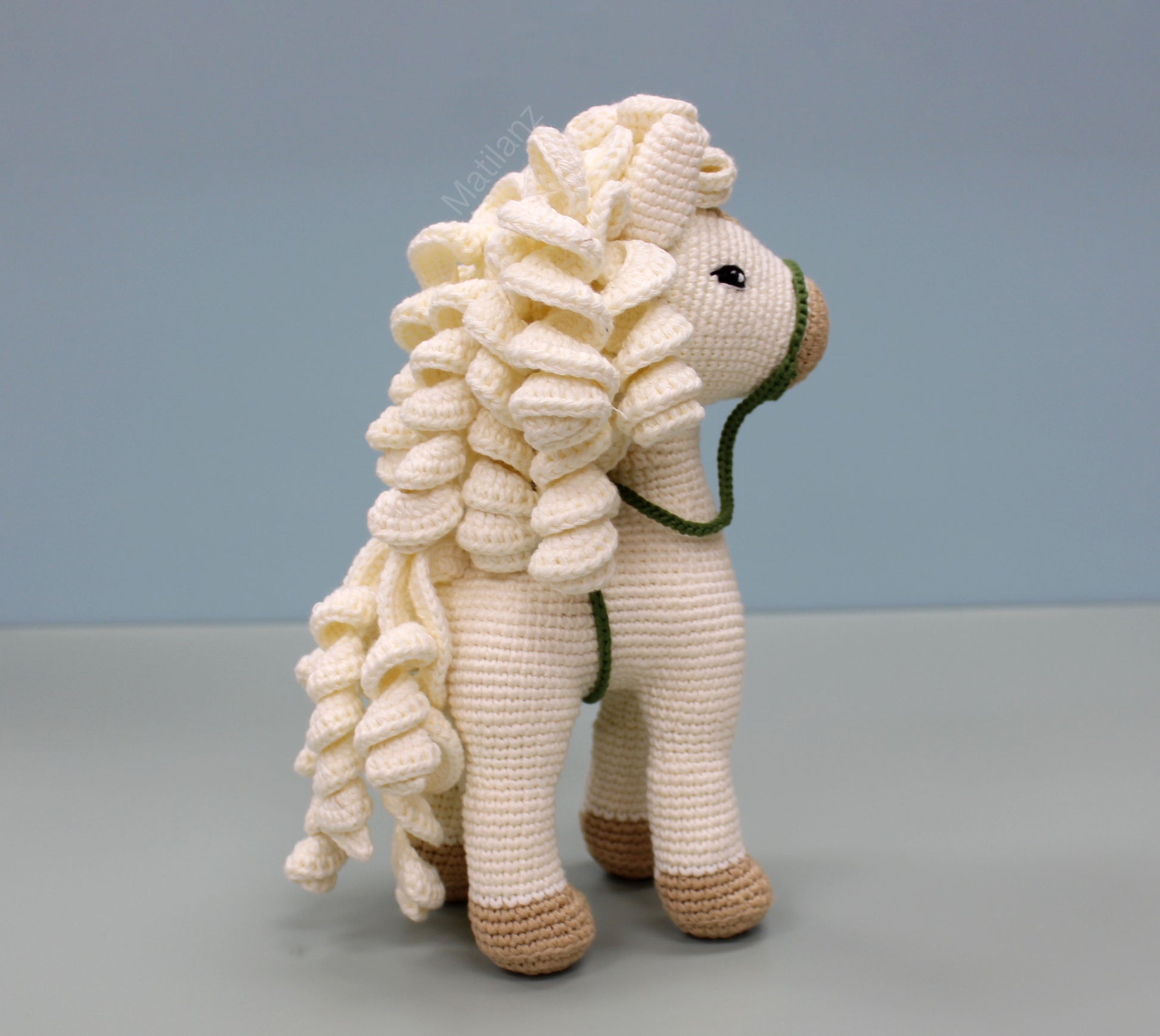 A handmade white cotton crochet horse toy, 10 inches tall, featuring a detailed mane and brown hoofs.
