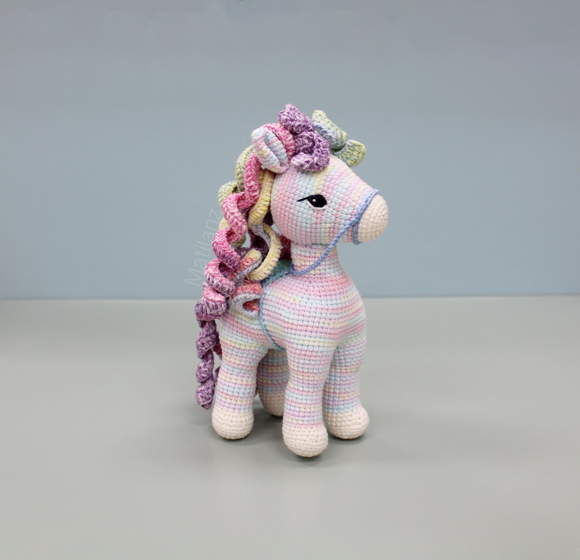 A handmade 9-inch crocheted rainbow horse with colorful yarn and large eyes.