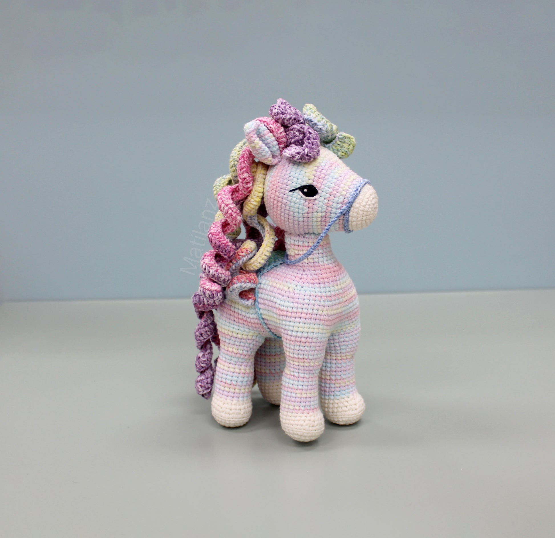 Colorful handmade crochet horse with rainbow mane and expressive eyes, approximately 9 inches tall.