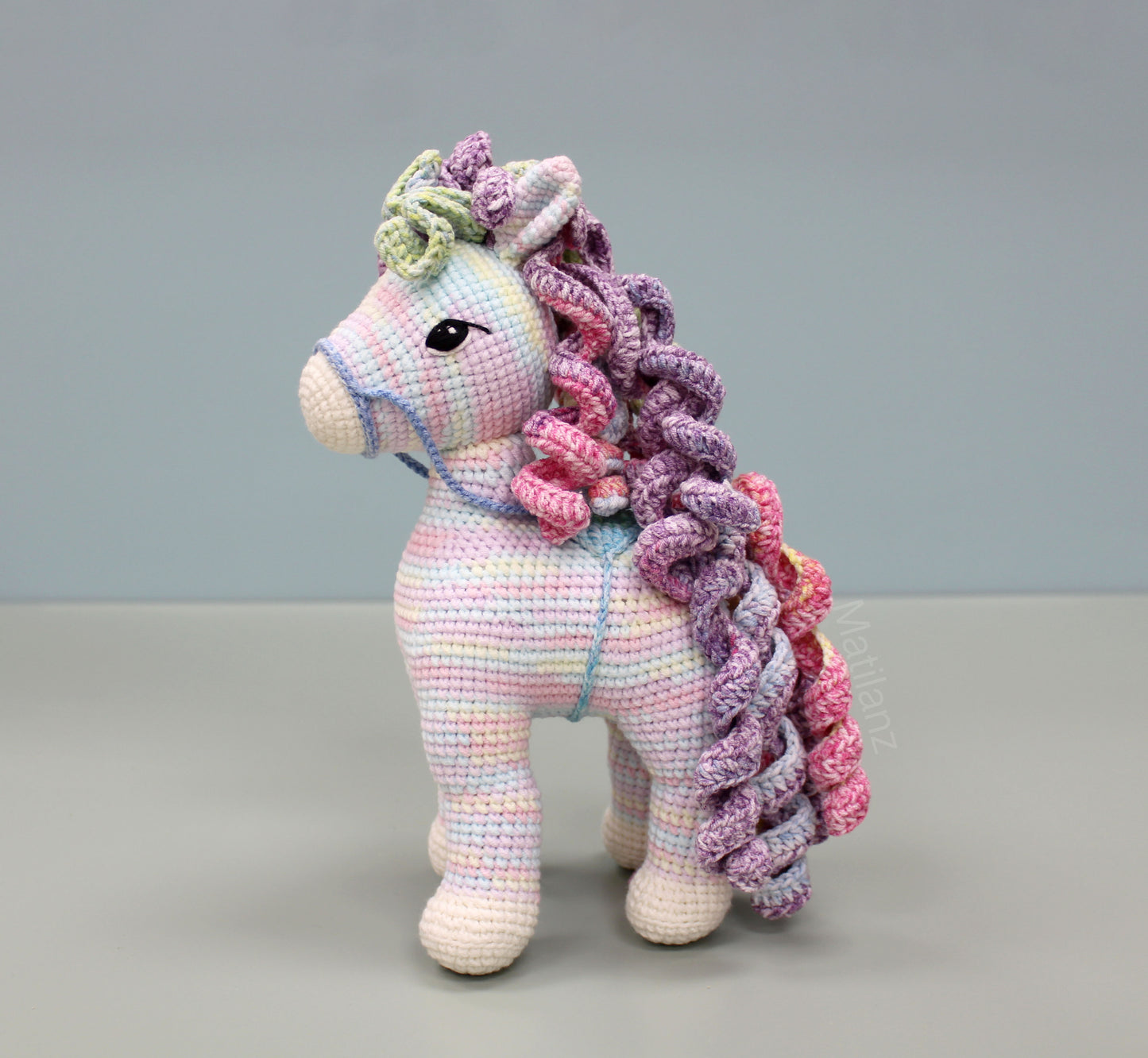A handmade 9-inch crochet rainbow horse with vibrant multicolored yarn and expressive black eyes.