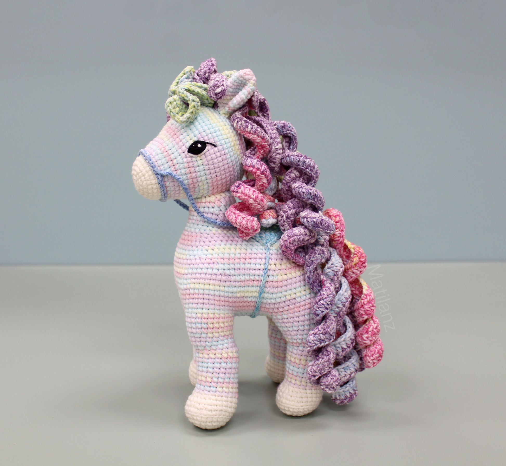 A handmade 9-inch crochet rainbow horse with vibrant multicolored yarn and expressive black eyes.