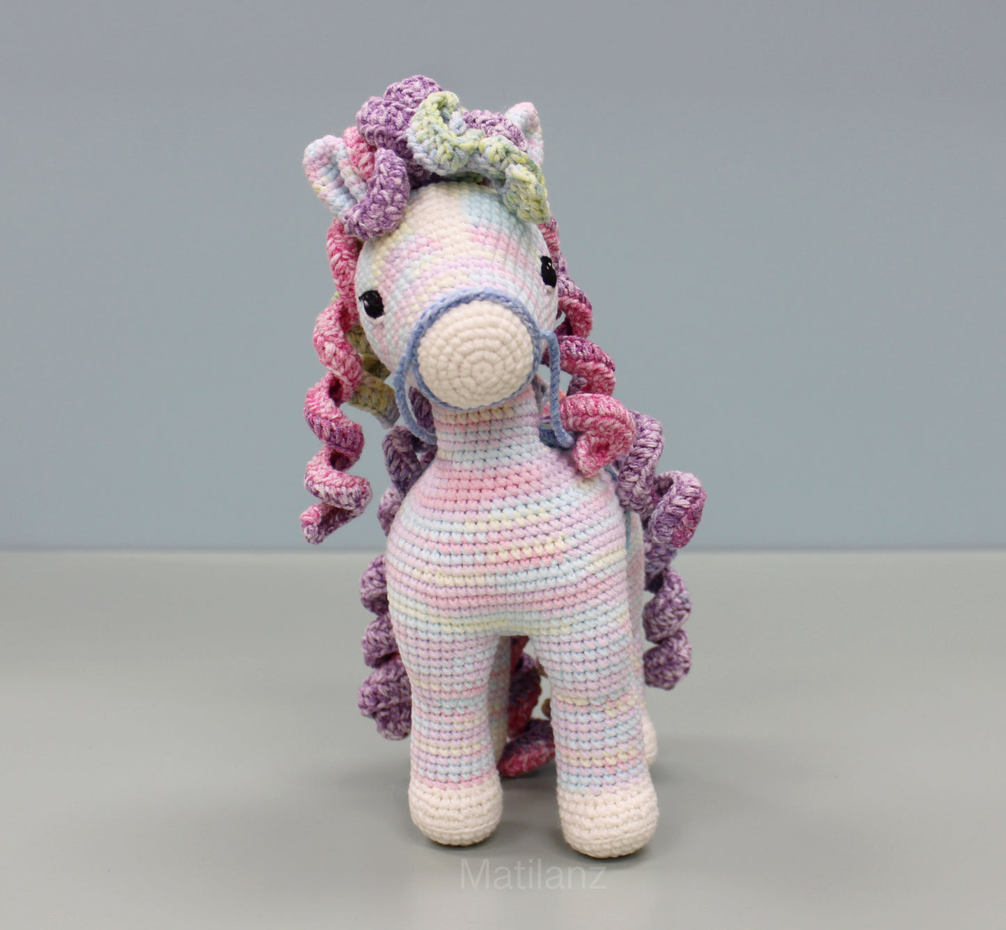 A handmade 9-inch crocheted rainbow horse with vibrant pastel colors and expressive black eyes.