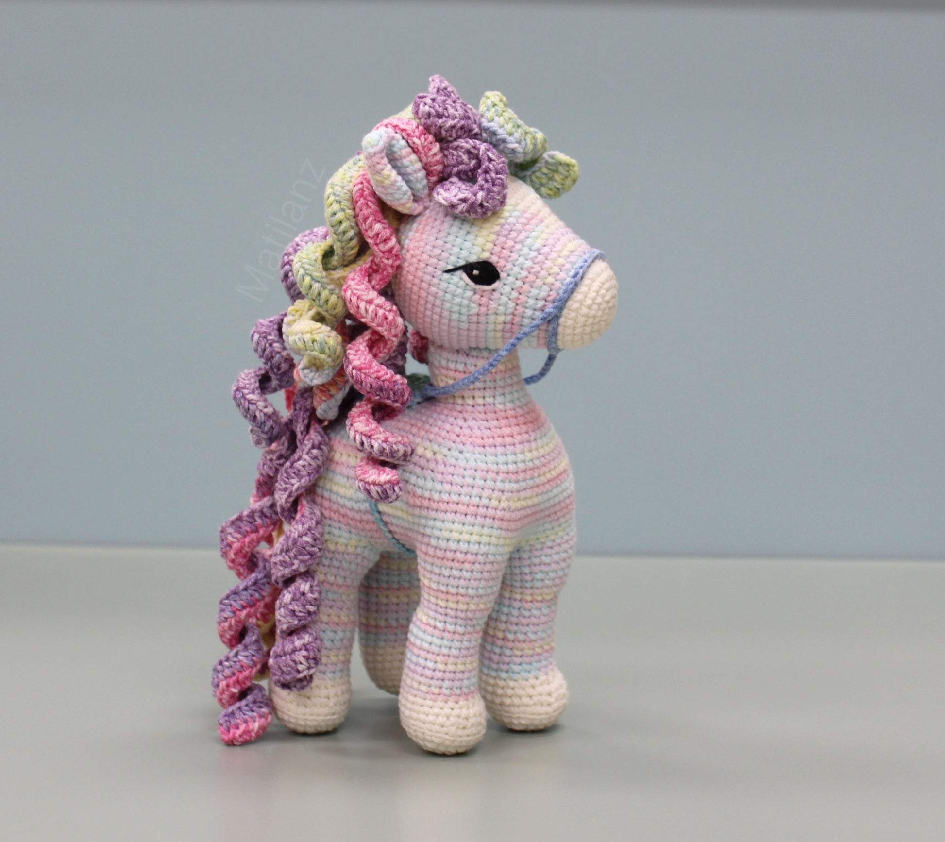 A handmade crocheted rainbow-colored horse with curly mane and tail, featuring detailed stitching and large expressive eyes.