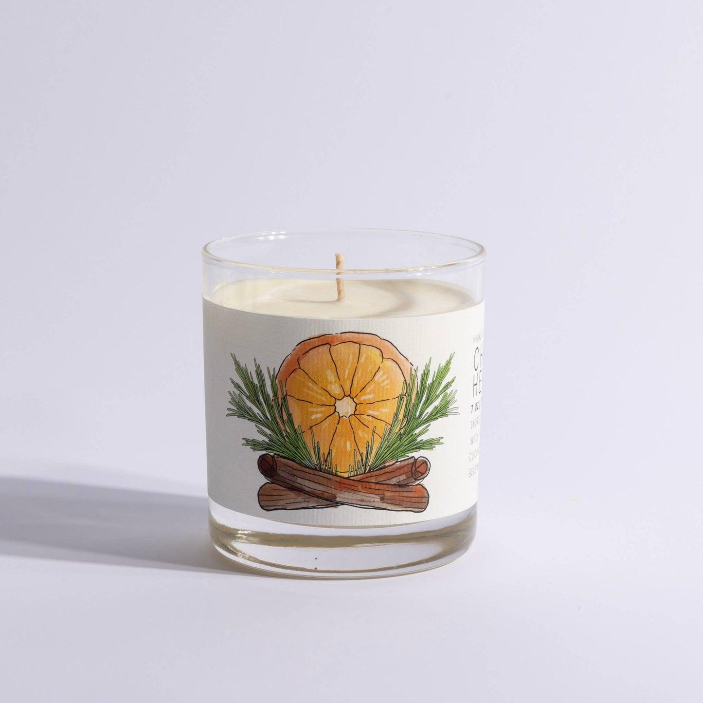 Medium glass candle with illustrated label of orange slice, pine, and cinnamon