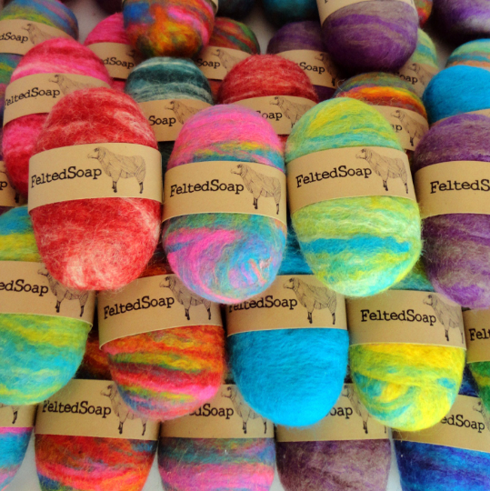 Vibrant multicolored felted soap bars, each wrapped with a natural label featuring a sheep illustration.