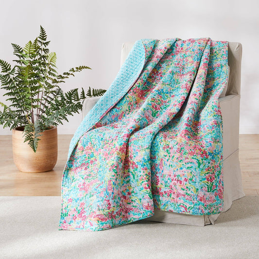 Bright floral quilted throw draped over a chair, reversible with teal pattern