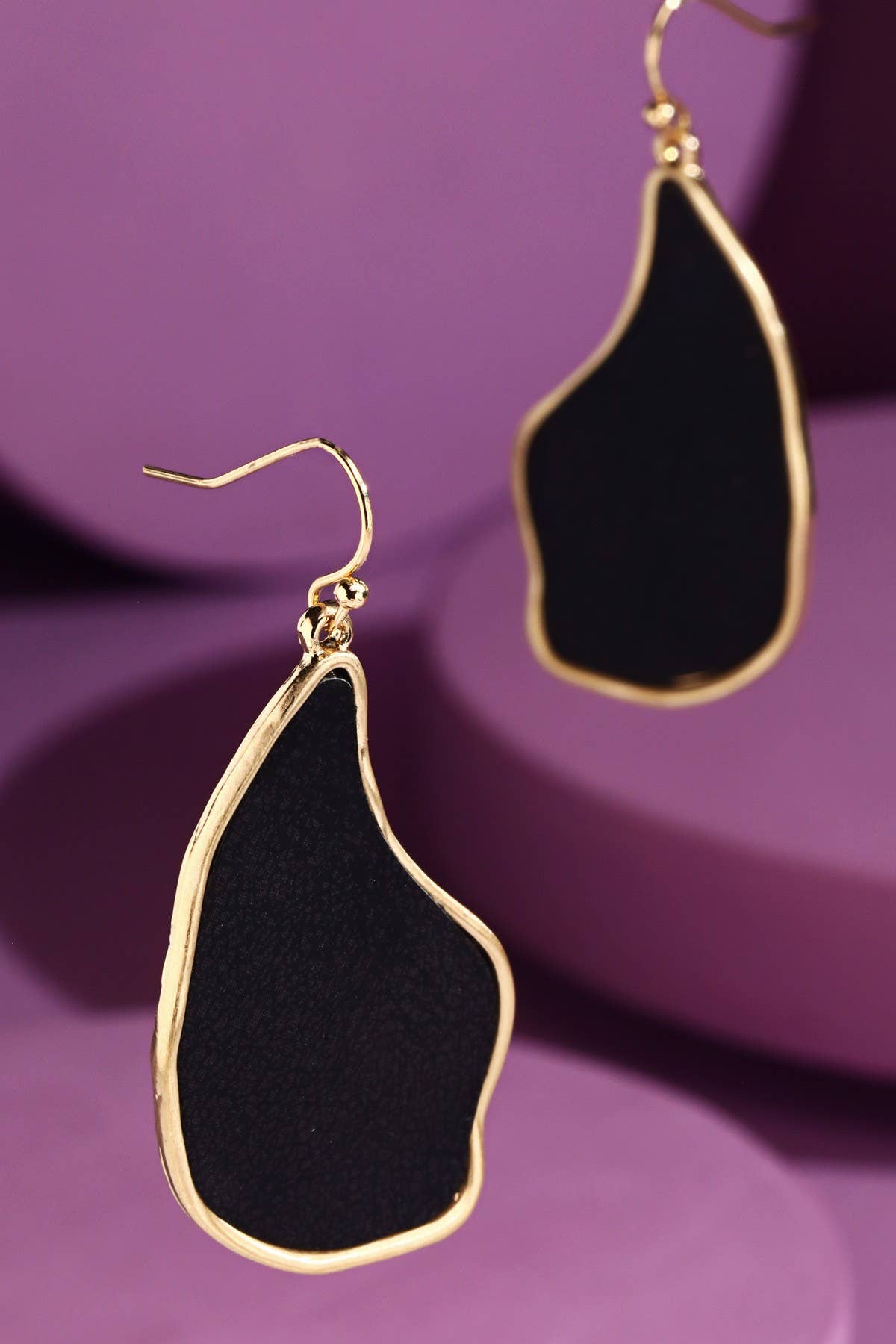 Black organic-shaped dangle earrings with gold trim on purple background