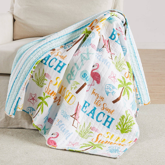 Colorful beach-themed quilted throw draped over a cream sofa