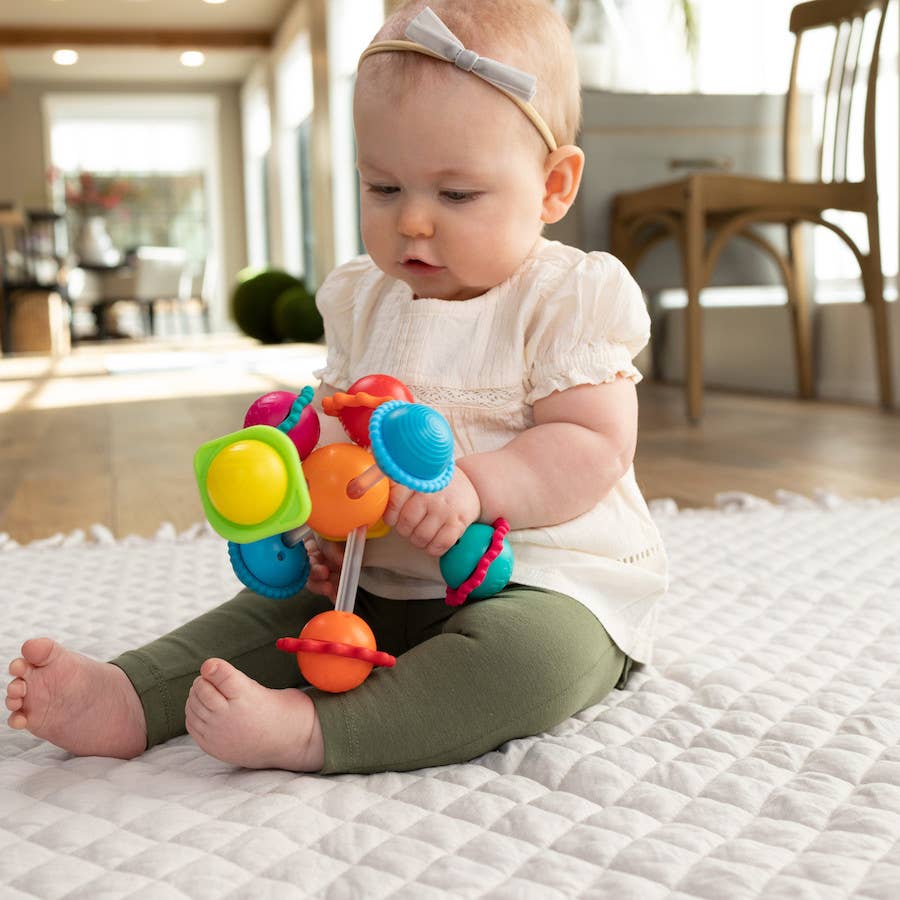 Baby exploring a colorful toy with spinning balls and silicone textures in a seated play position.