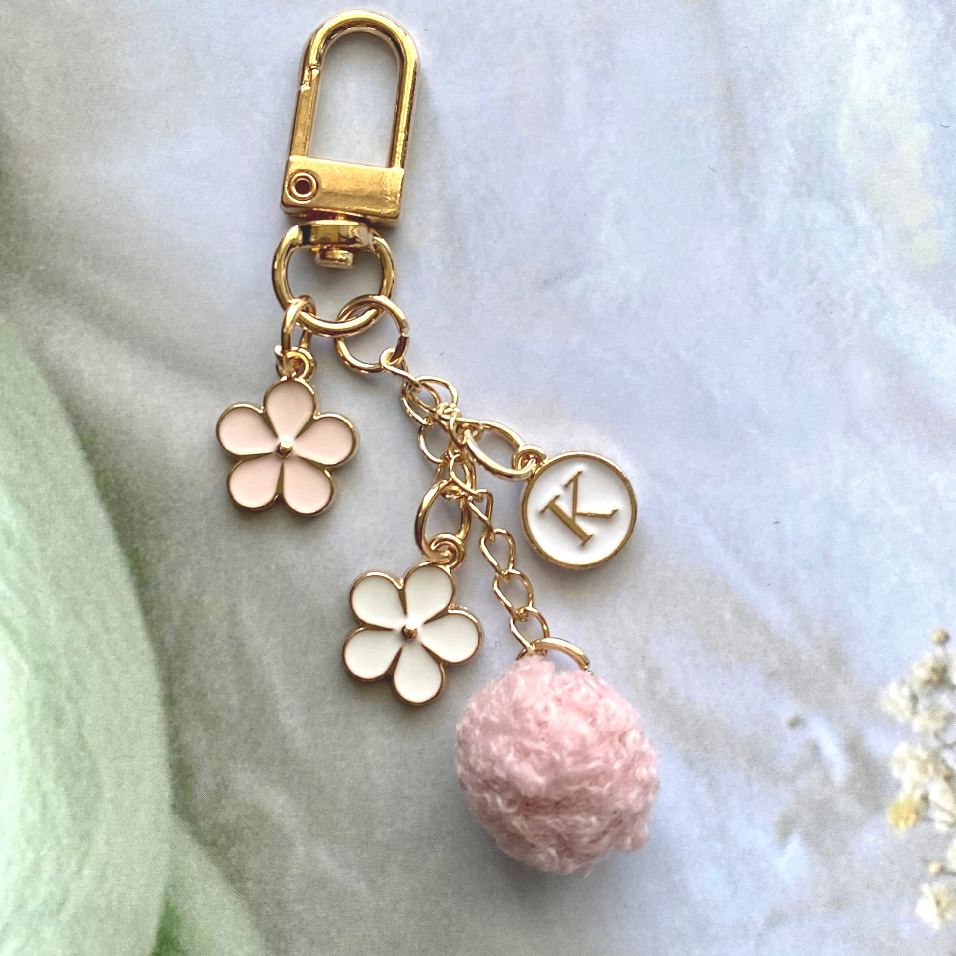Gold keychain with pink and white floral charms, initial letter K, and pink pompom