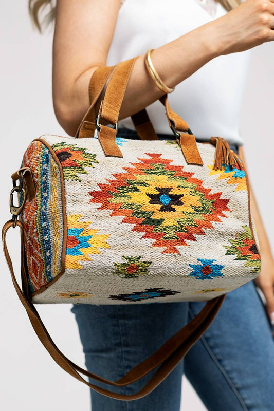 Ethnic-style Boston bag with geometric patterns and warm colors, featuring suede leather handles and a tassel accent.
