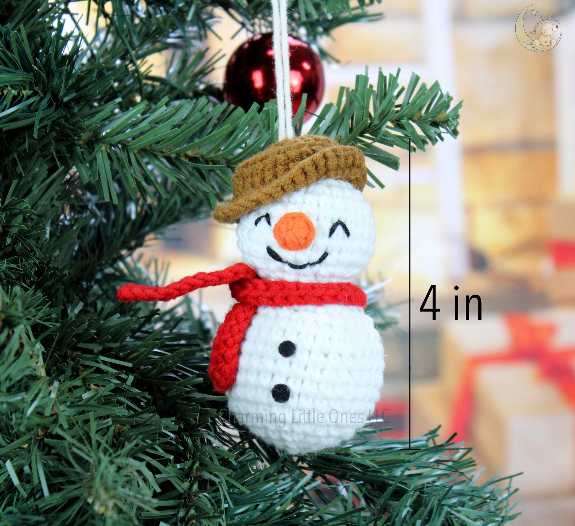 A handmade crochet Christmas snowman ornament with a brown hat, red scarf, and orange nose, hanging on a tree.