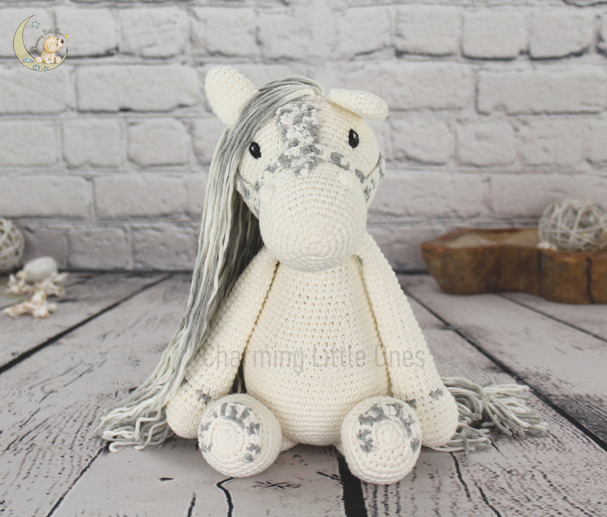A handmade crochet horse with long gray mane, cream body, and decorative details.