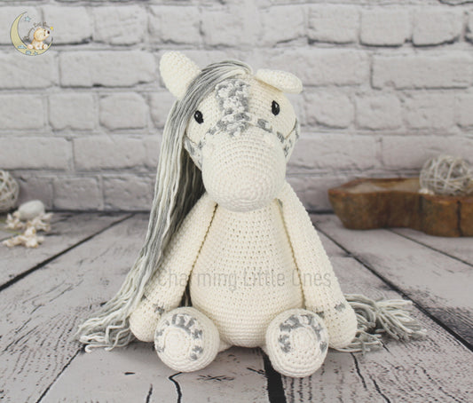 A handmade crochet horse with long gray mane, cream body, and decorative details.