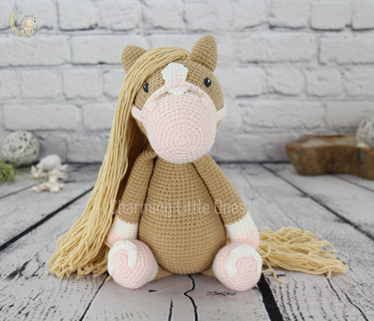 A handmade crochet horse with long blonde hair, pink accents, and a soft beige body.