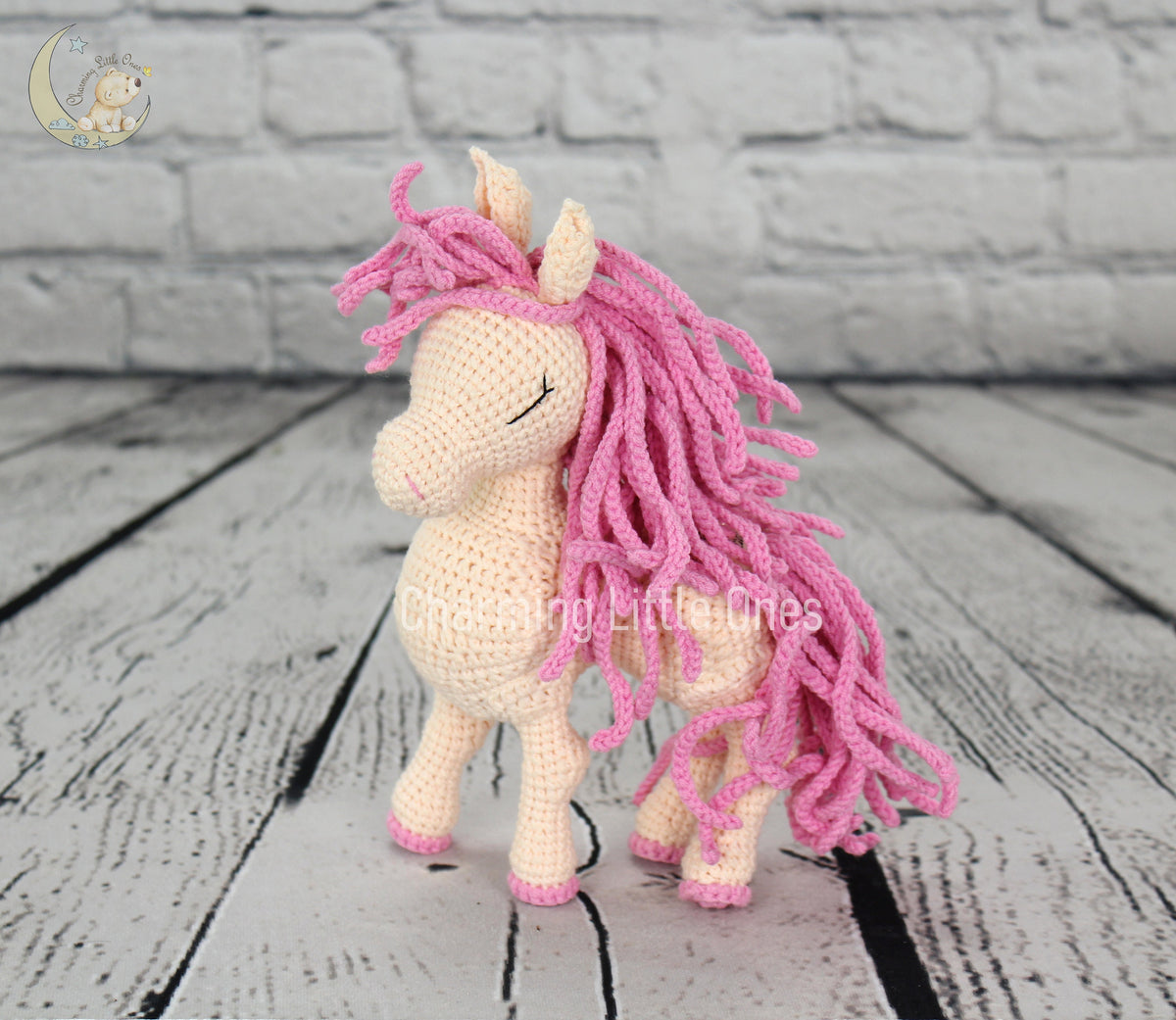 A handmade crochet horse with a pink mane and tail, standing on a wooden surface.