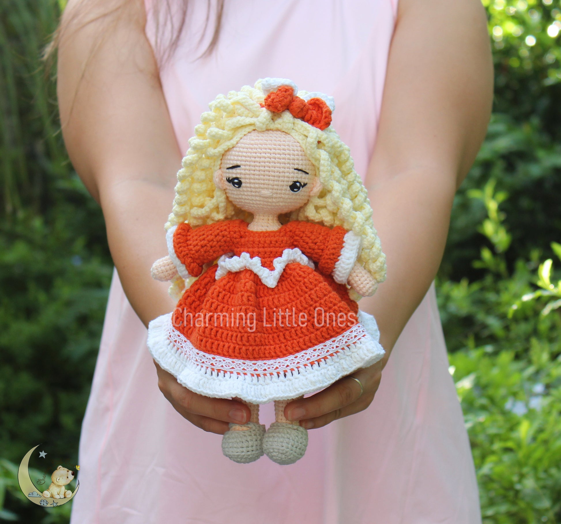 A handmade crochet doll with blonde hair, orange dress, and white lace trim.