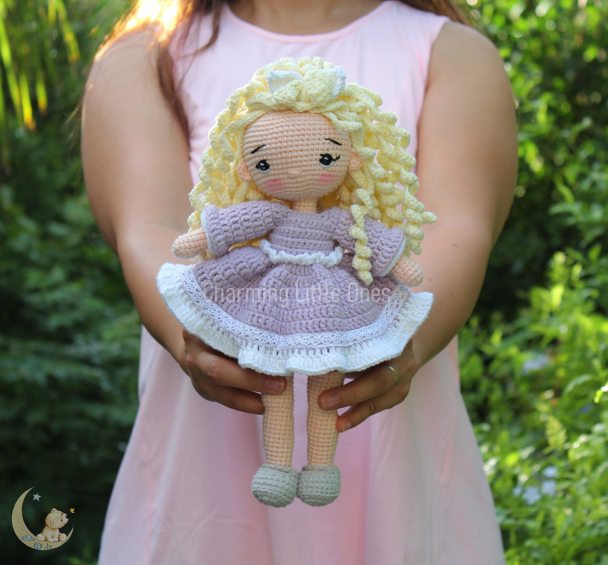 A handmade crochet doll with long blonde hair, wearing a lavender dress with white lace trim.