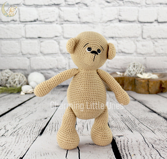 A handmade crochet bear with a beige color, standing on a wooden surface.