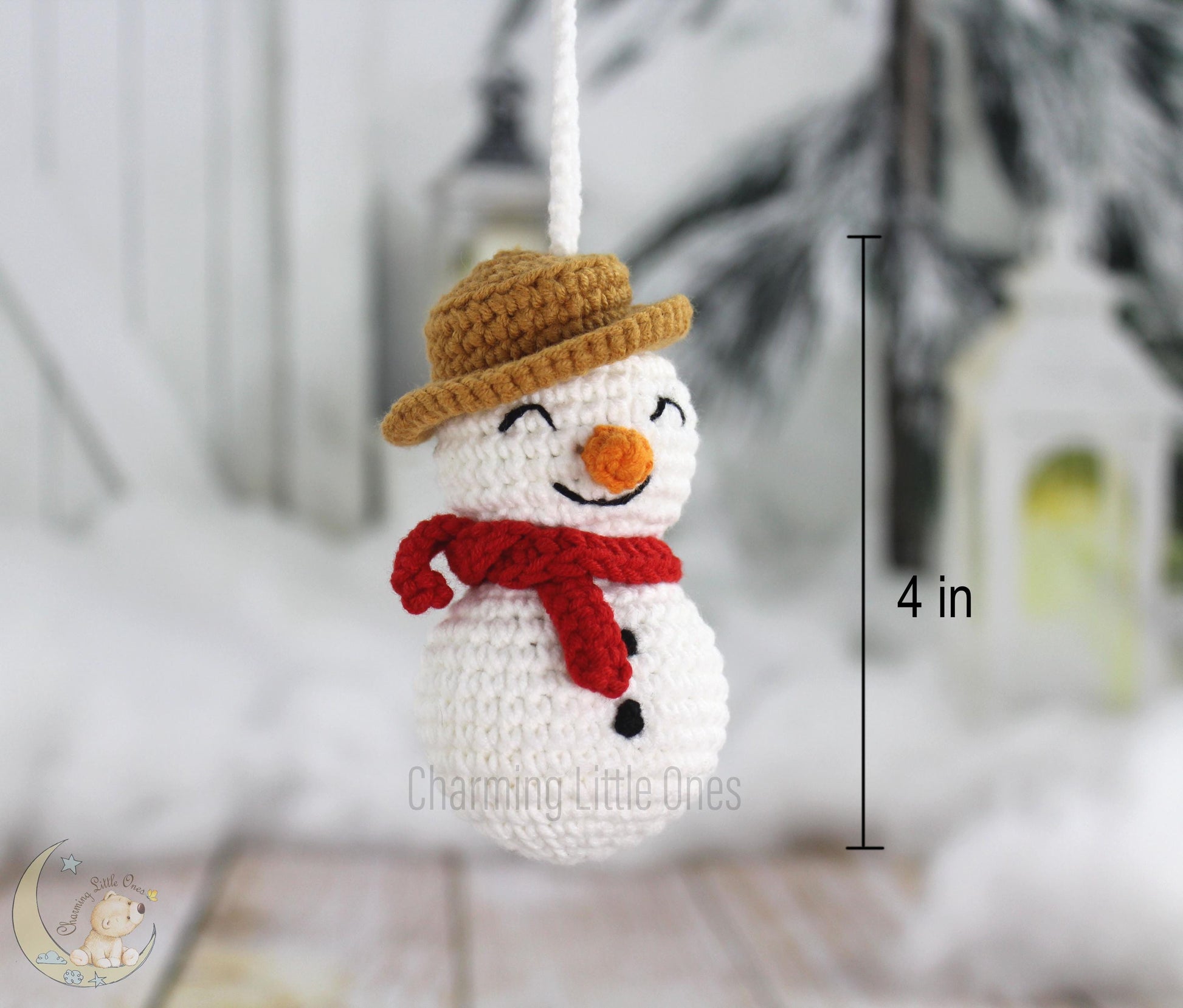 A handmade crochet snowman ornament with a brown hat, red scarf, and orange nose, 4 inches tall.