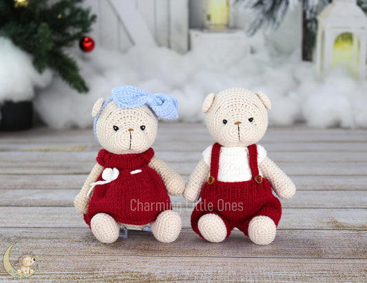 Two handmade crochet Christmas bears, one in a red dress with a blue bow, the other in red overalls, sitting on a wooden surface.