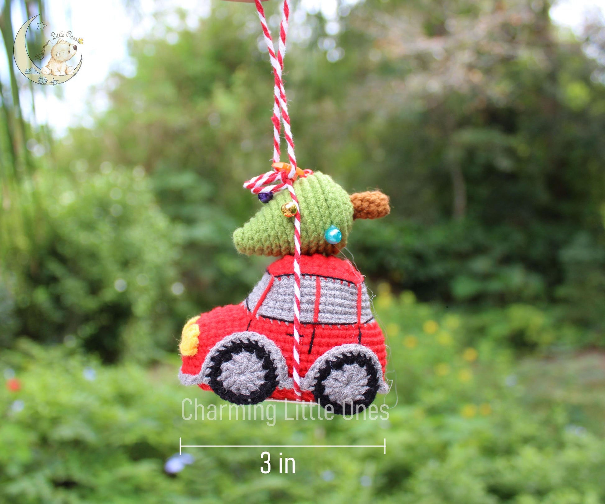 A handmade crochet red car Christmas ornament with a green tree on top, featuring gray wheels and yellow accents.