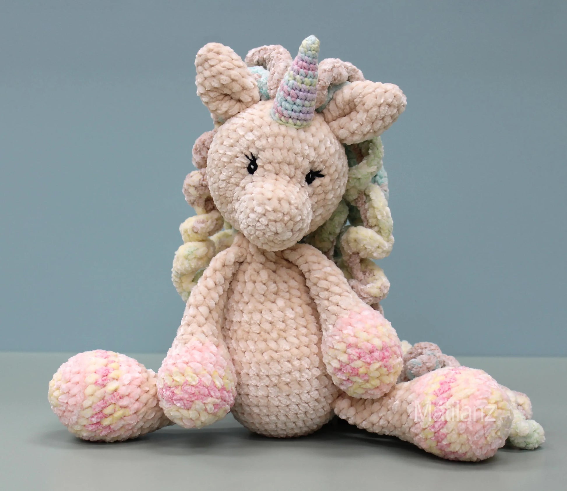 Hand-crocheted plush unicorn with rainbow mane and pink hooves