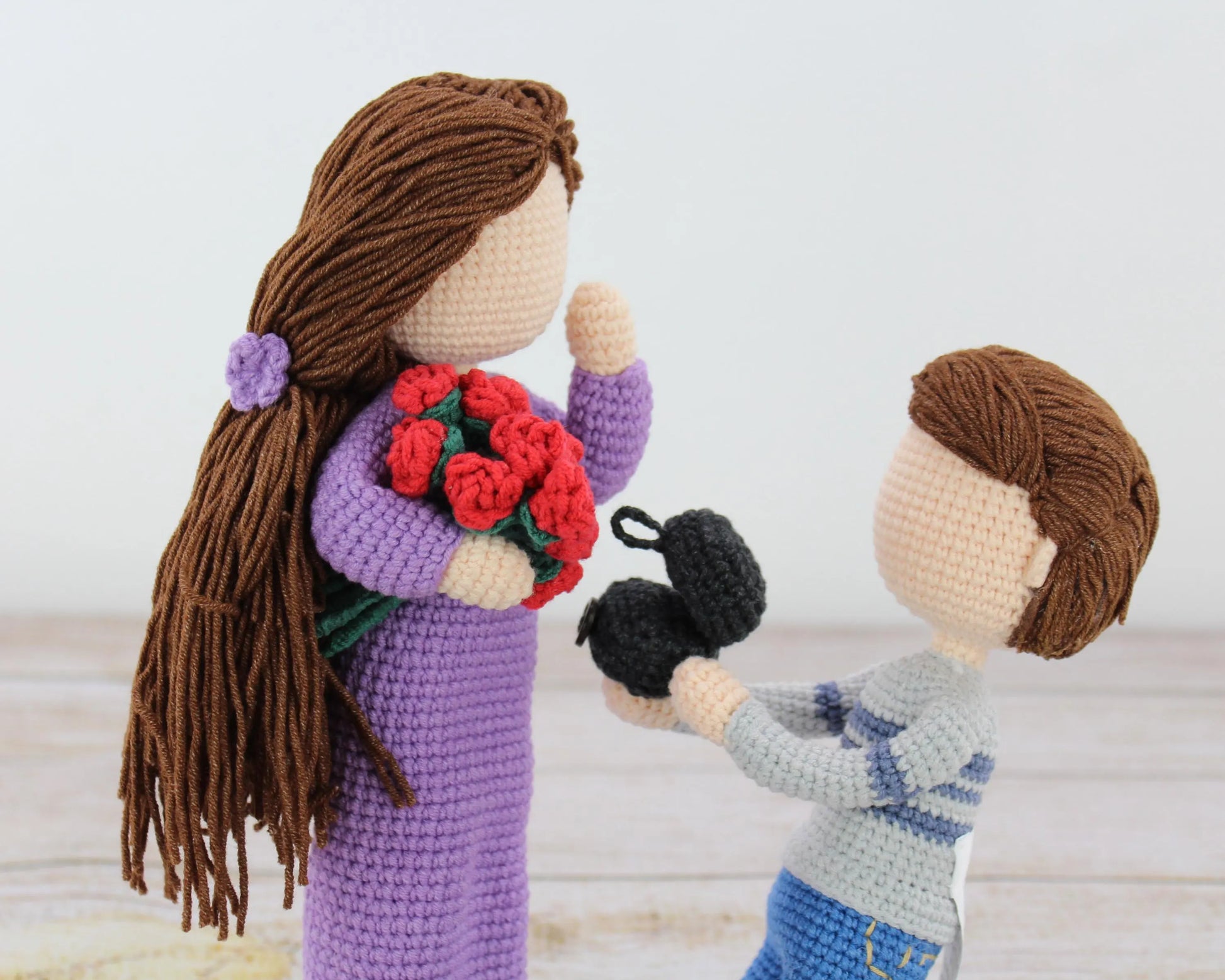 Handmade crochet dolls, one holding a bouquet of red roses and the other offering blackberries.
