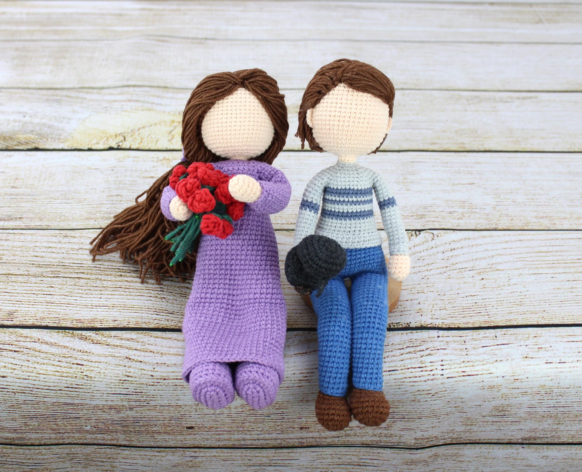 Handmade crocheted dolls, one in purple dress holding flowers, the other in blue striped sweater and jeans.