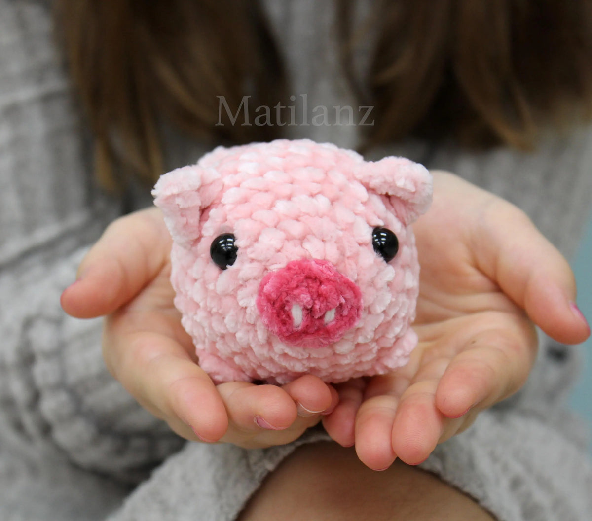 A cute pink crochet plush pig with shiny black eyes and a snout, perfect for cuddling.