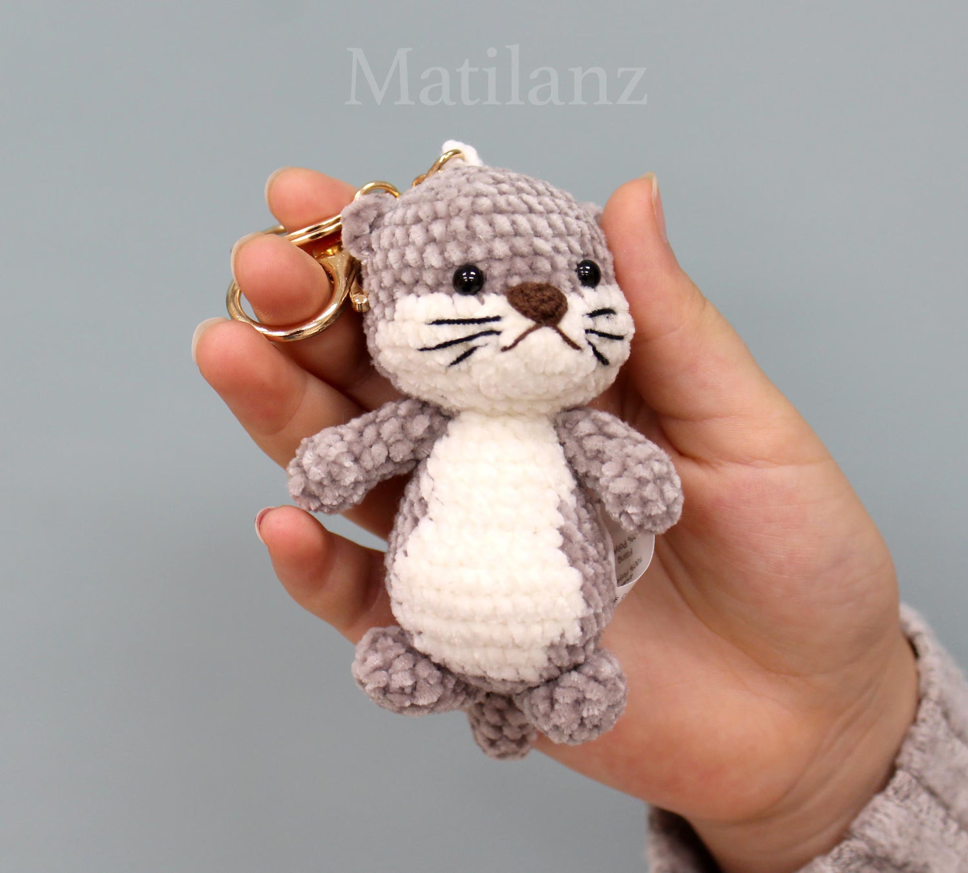 Crochet otter keychain with gray and white fur, black eyes, and a brown nose.