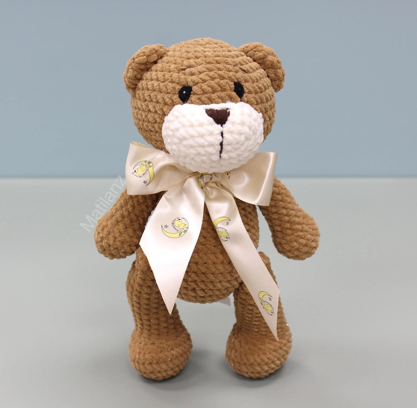 A handmade brown crochet bear with a white muzzle and a light beige bow.