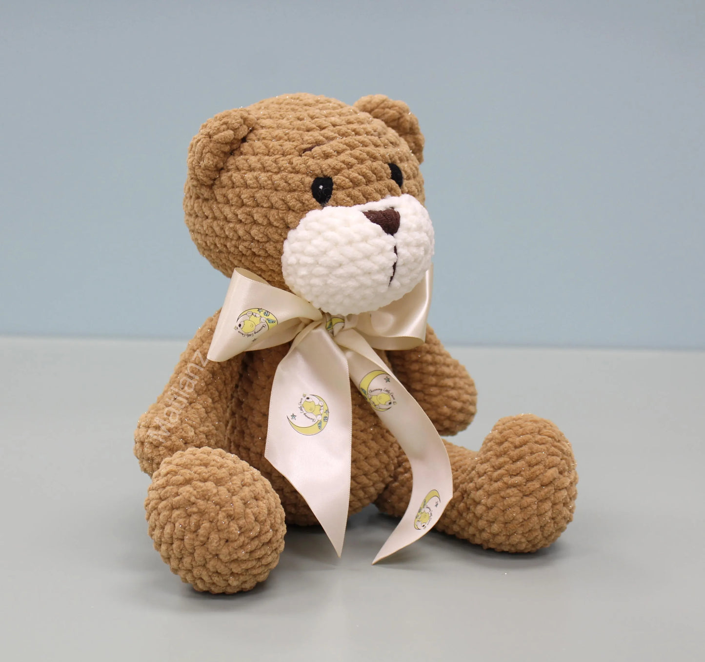 Handmade crochet teddy bear with a soft brown texture and cream-colored bow.