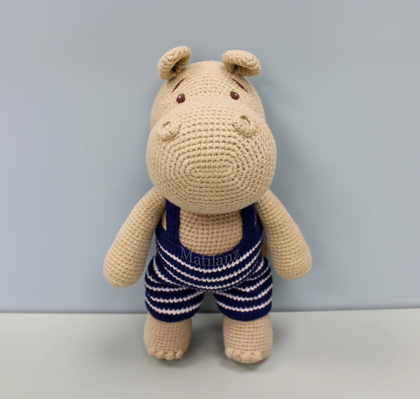 Crocheted hippo plushie in a blue and white striped swimsuit.