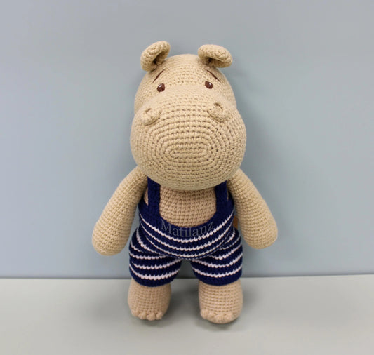 Crocheted hippo plushie in a blue and white striped swimsuit.