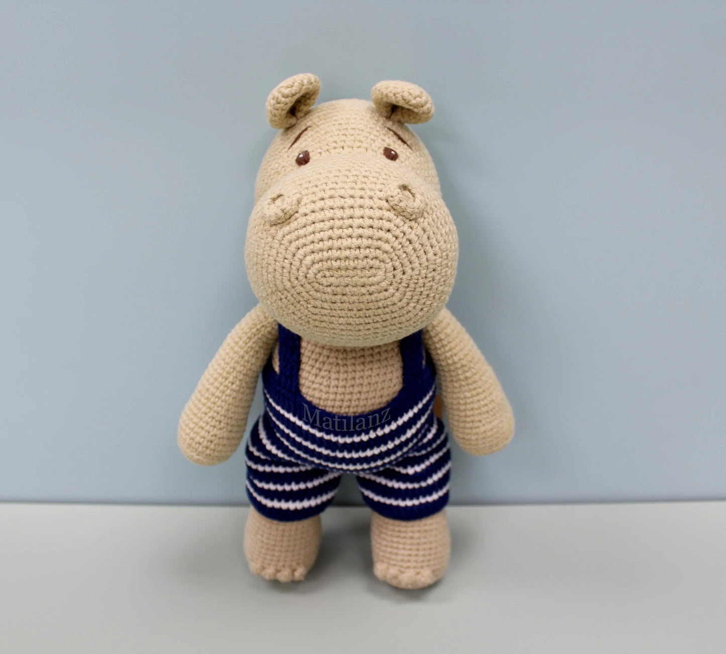 Crocheted beige hippo plushie wearing a blue and white striped swimsuit.