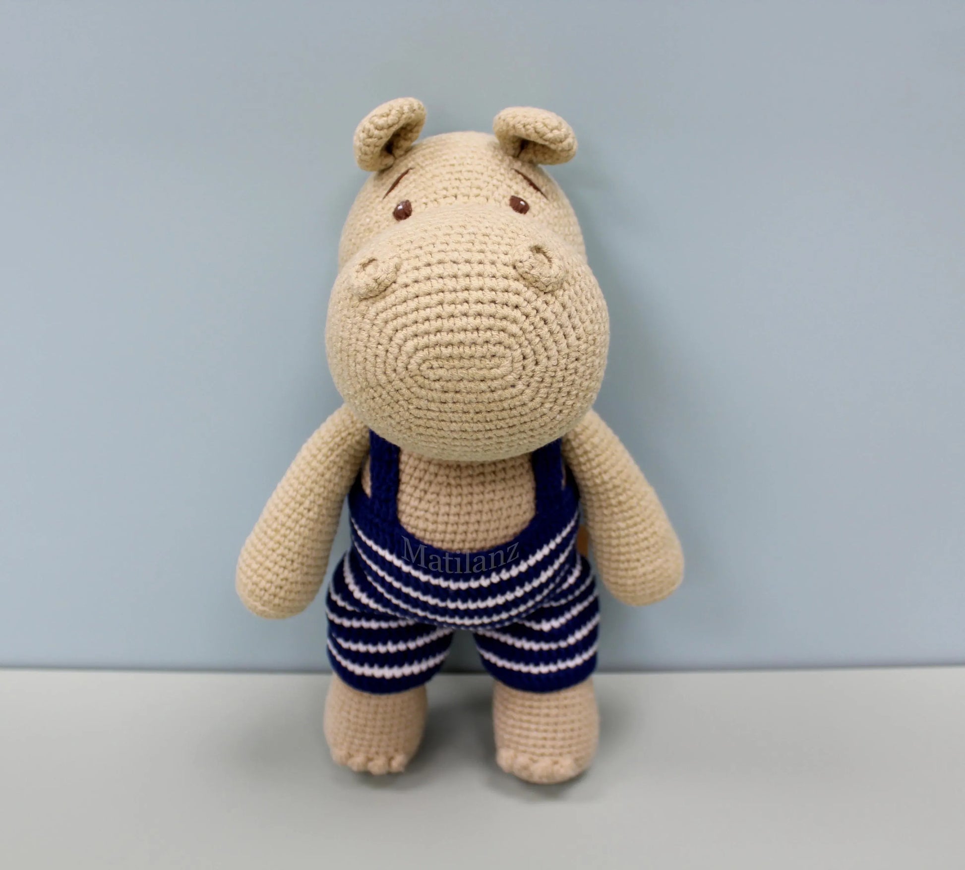 Crocheted beige hippo plushie wearing a blue and white striped swimsuit.