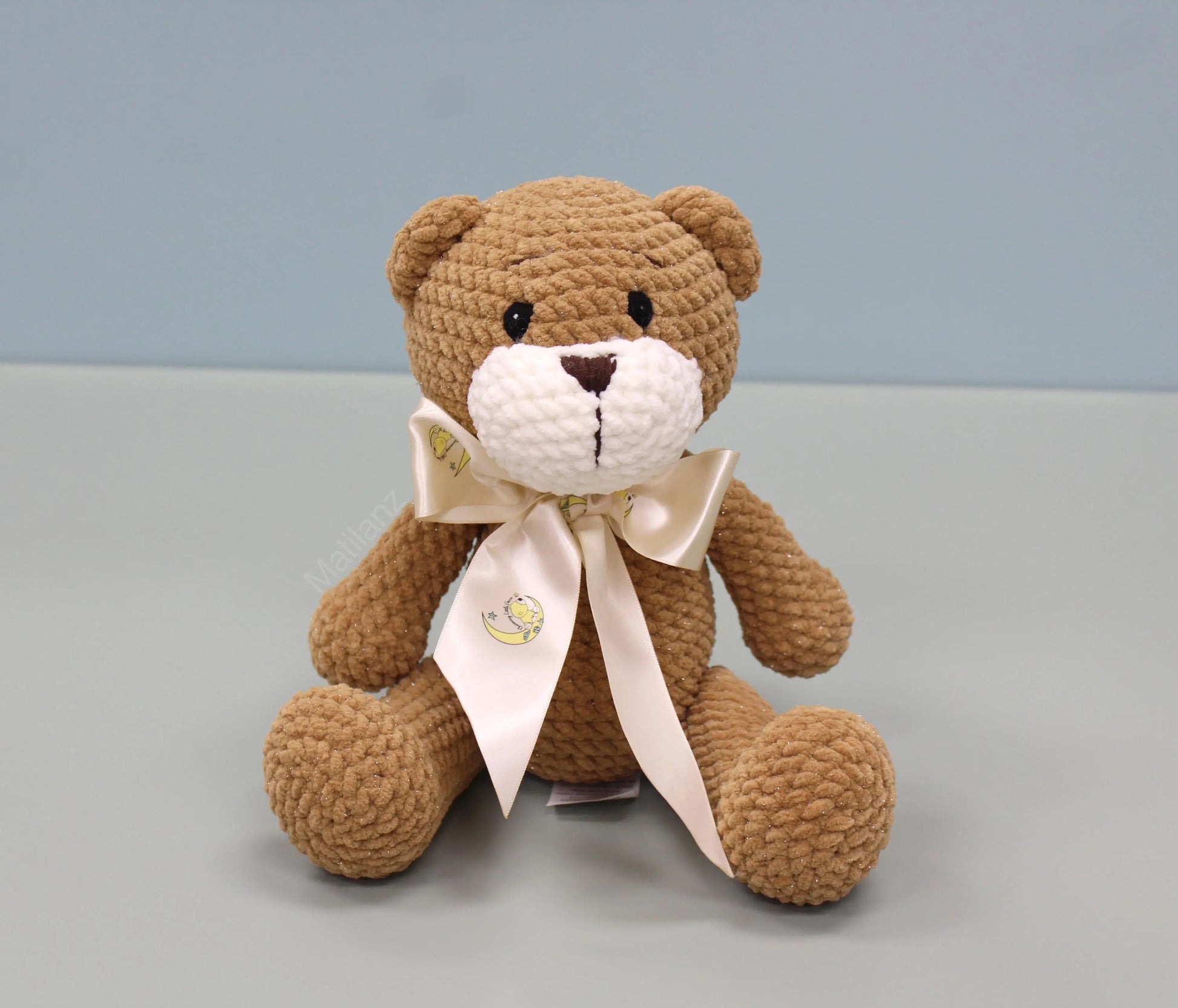 Brown crochet teddy bear with a cream satin bow featuring a moon and stars design.