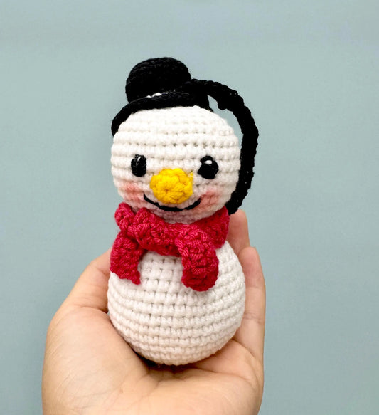 Crochet snowman ornament with a black hat, red scarf, and cheerful yellow nose.