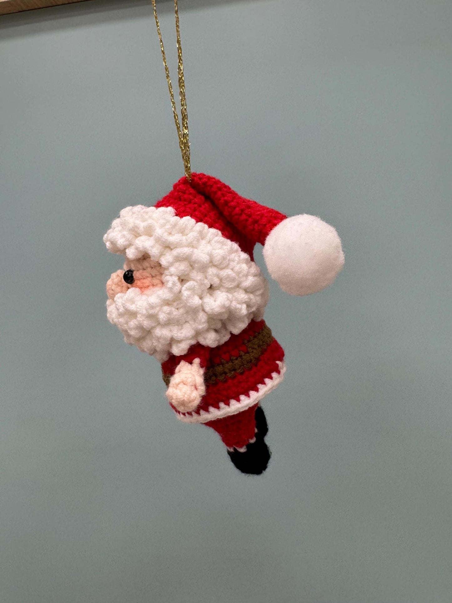 Crochet Santa Claus ornament with red and white outfit, black boots, and a fluffy white beard.