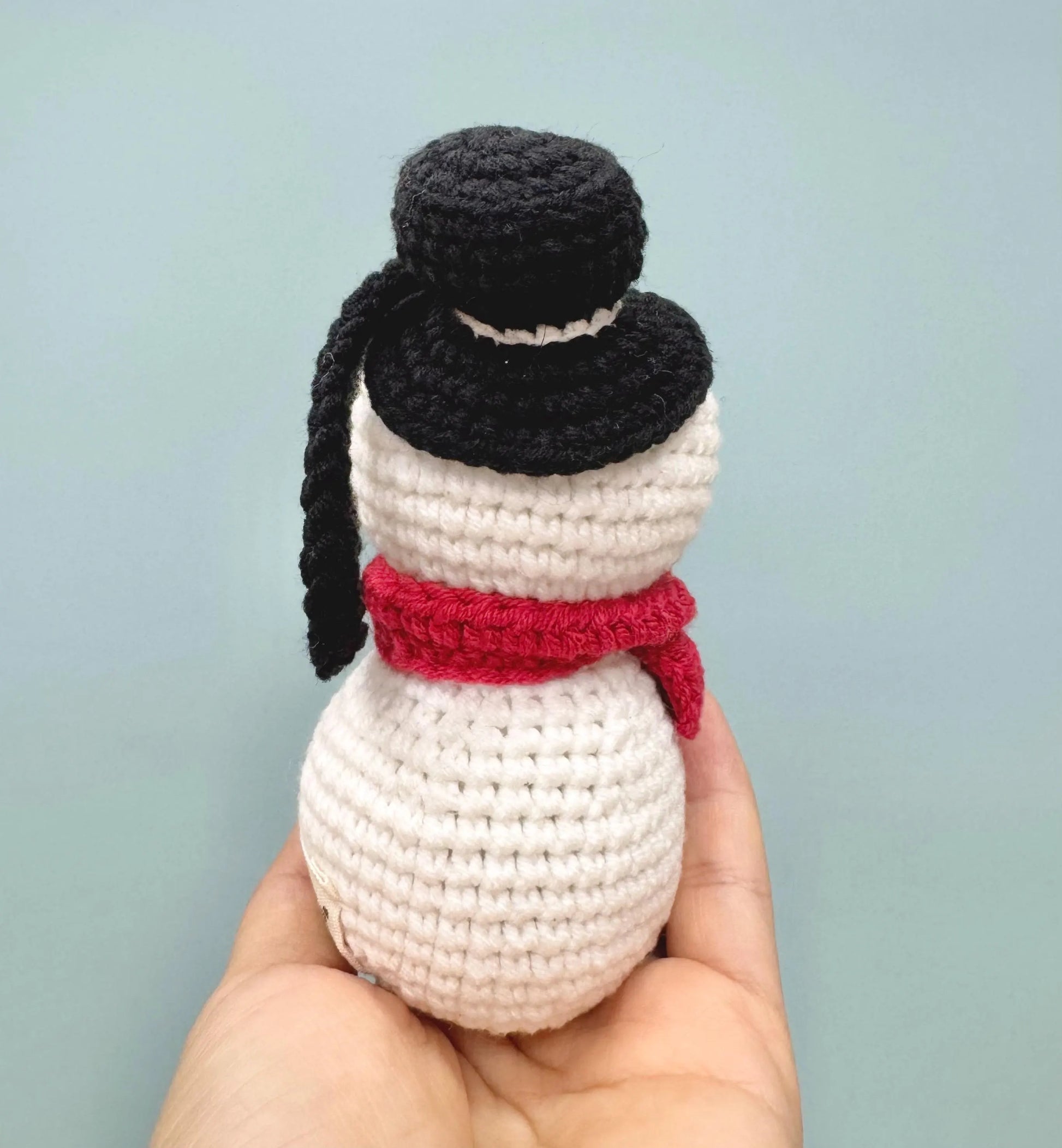 Crochet snowman ornament with a black top hat and red scarf, perfect for festive decorating.