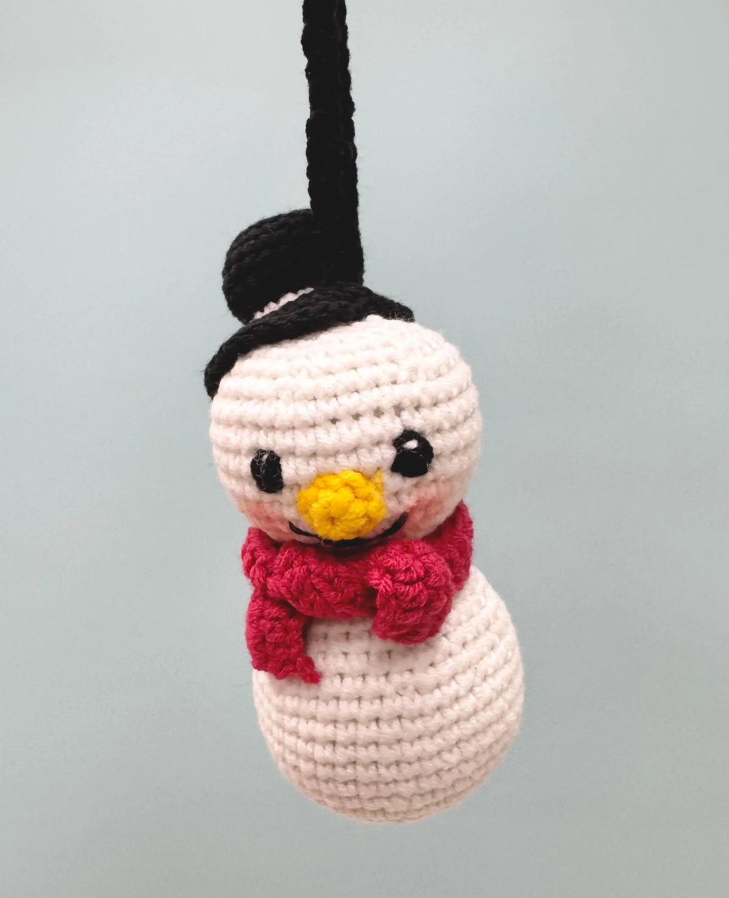 Crochet snowman ornament with a black hat, yellow nose, and red scarf, perfect for festive decorating.