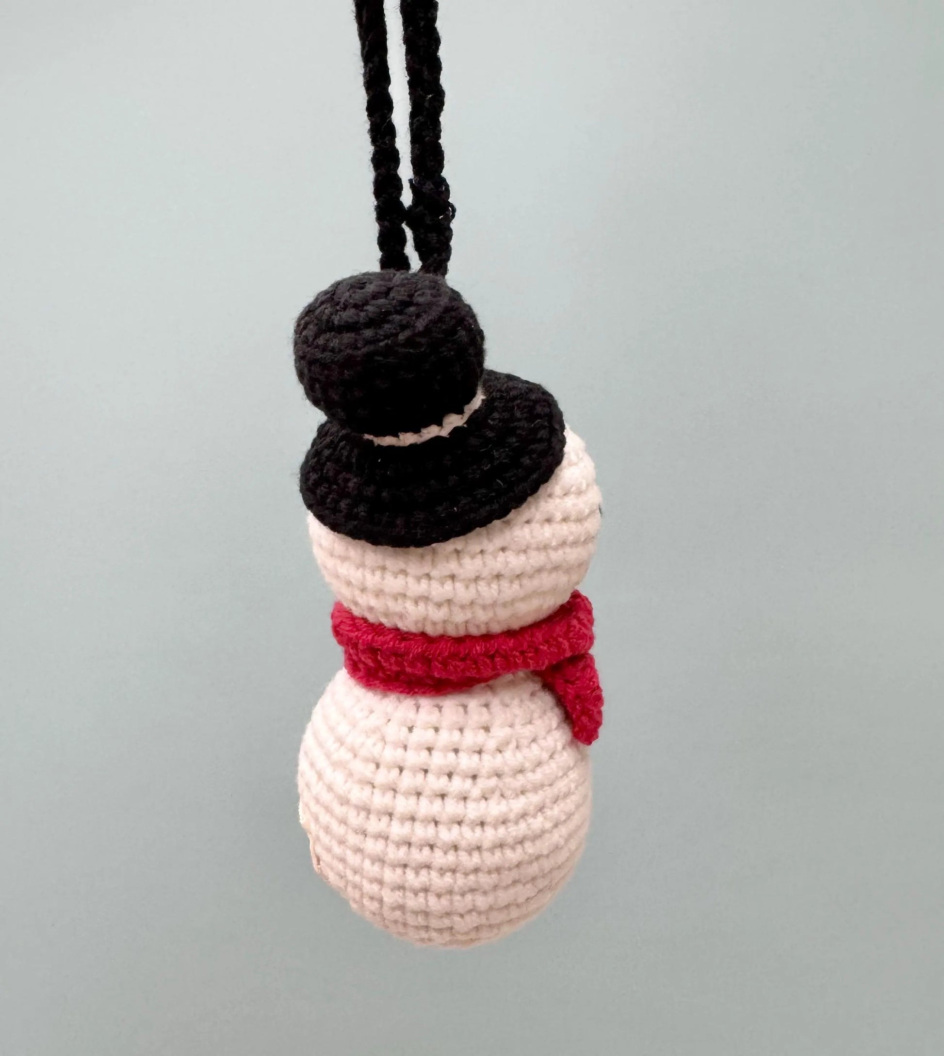 Crochet snowman ornament with a black hat and red scarf, perfect for festive decorating.
