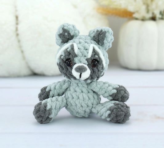Crochet raccoon plush in soft gray and white, featuring a cute face and fluffy texture.