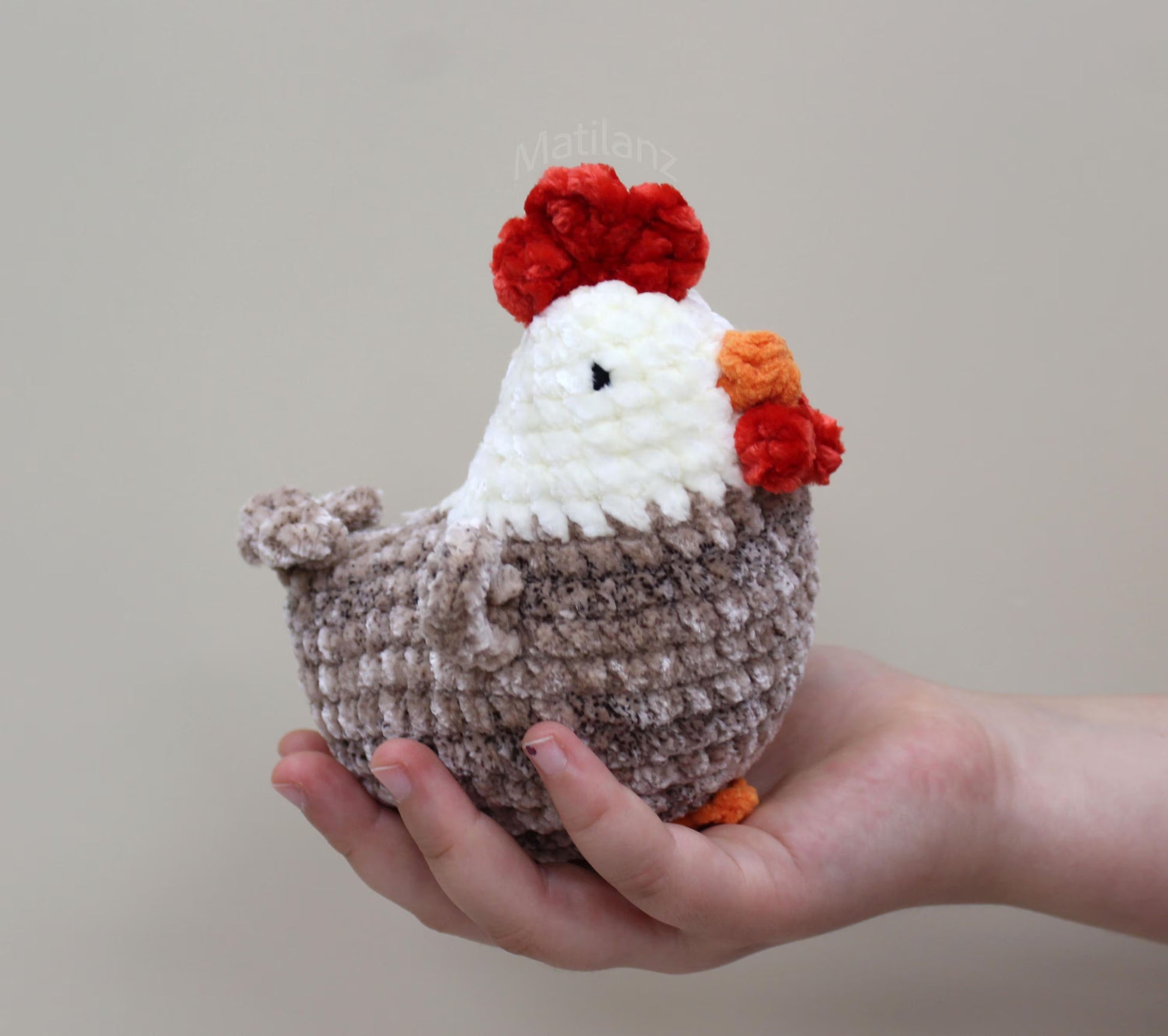 A handmade crochet chicken plushie with beige, white, and red yarn, featuring a fluffy texture and a red comb.