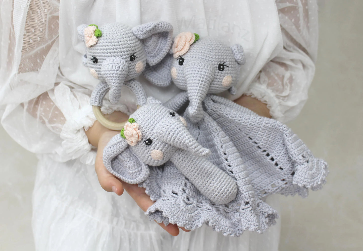 Hand-crocheted gray elephant rattle toys with floral accents and a matching blanket.