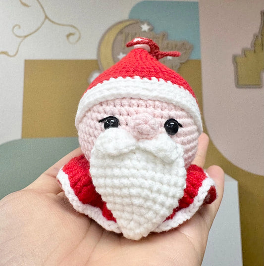 Cute crochet Santa Claus ornament with a red hat, white beard, and rosy cheeks, perfect for holiday decorating.
