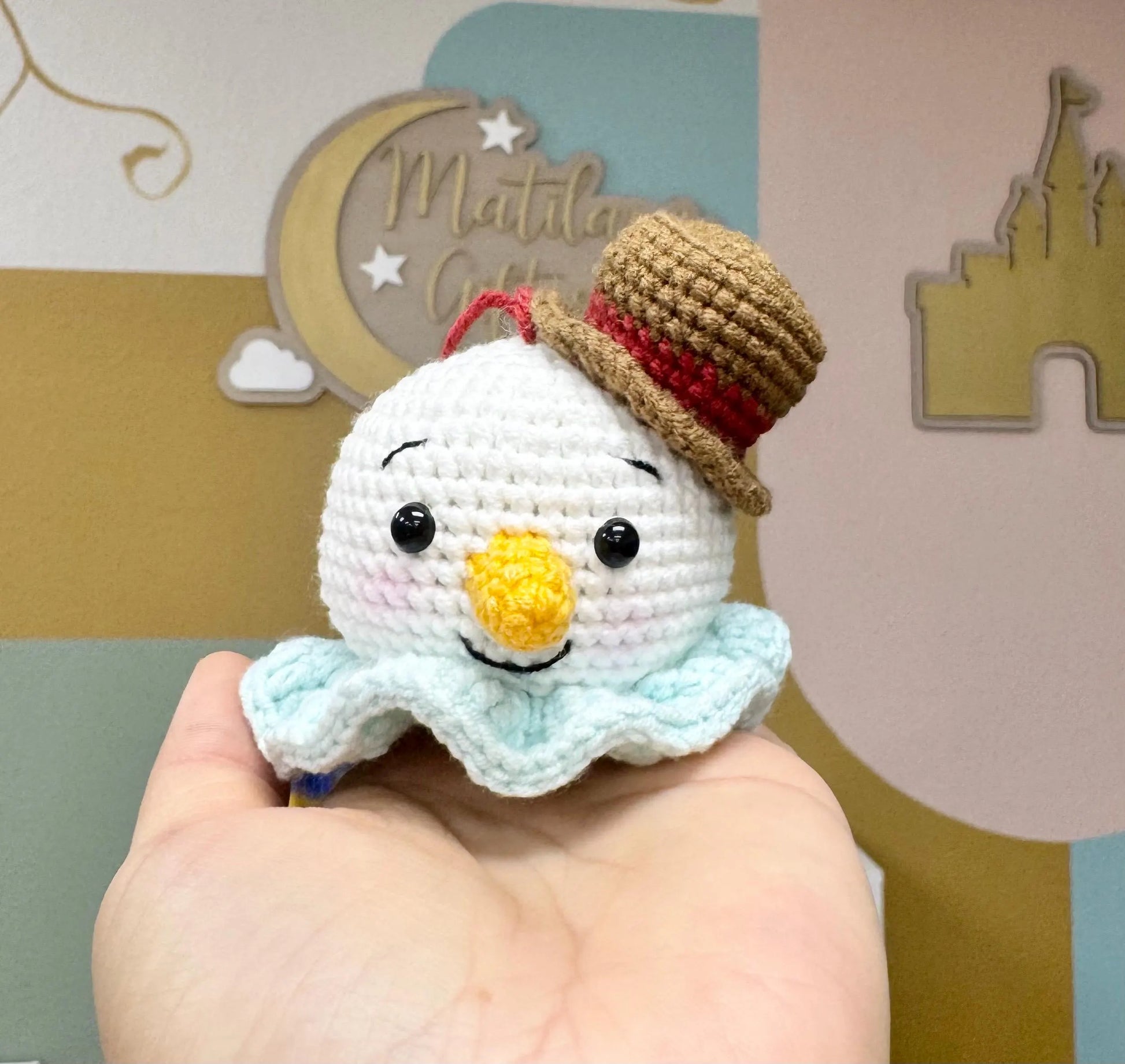 Cute crochet snowman ornament with a brown hat, yellow nose, and blue scarf.